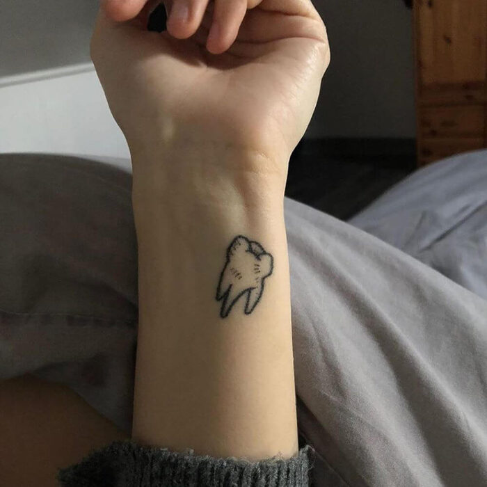 Tattoo of a tooth on a wrist